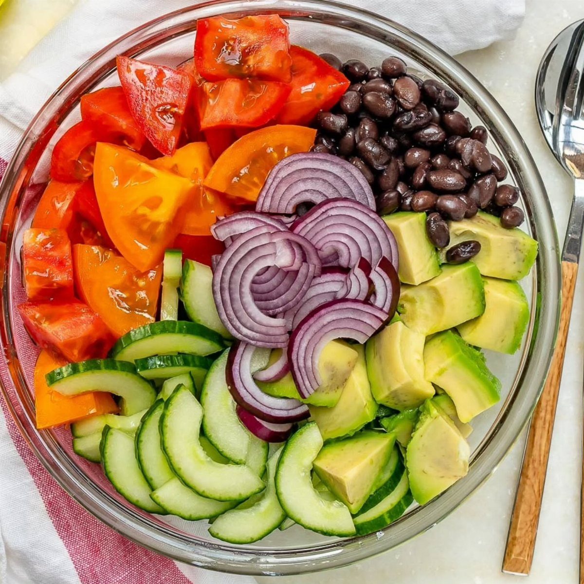 Colorful bowl of tomatoes, black beans, cucumber, avocado, and purple onion