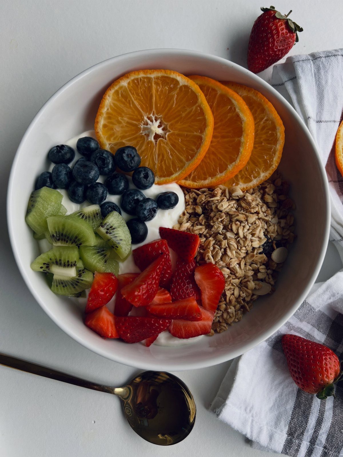 Fruit and granola arranged over yogurt in a white bowl beside a spoon