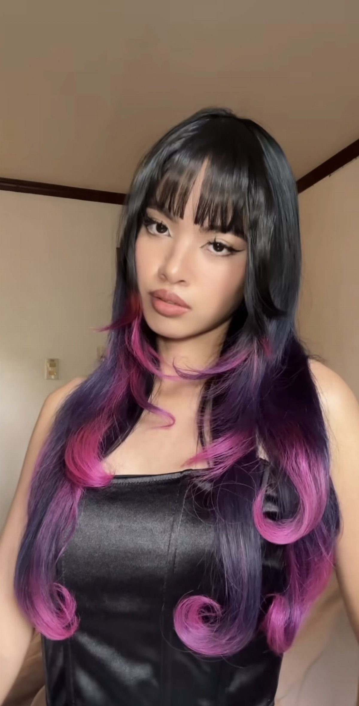 Woman with blunt bangs and long black hair ending in purple-pink spirals