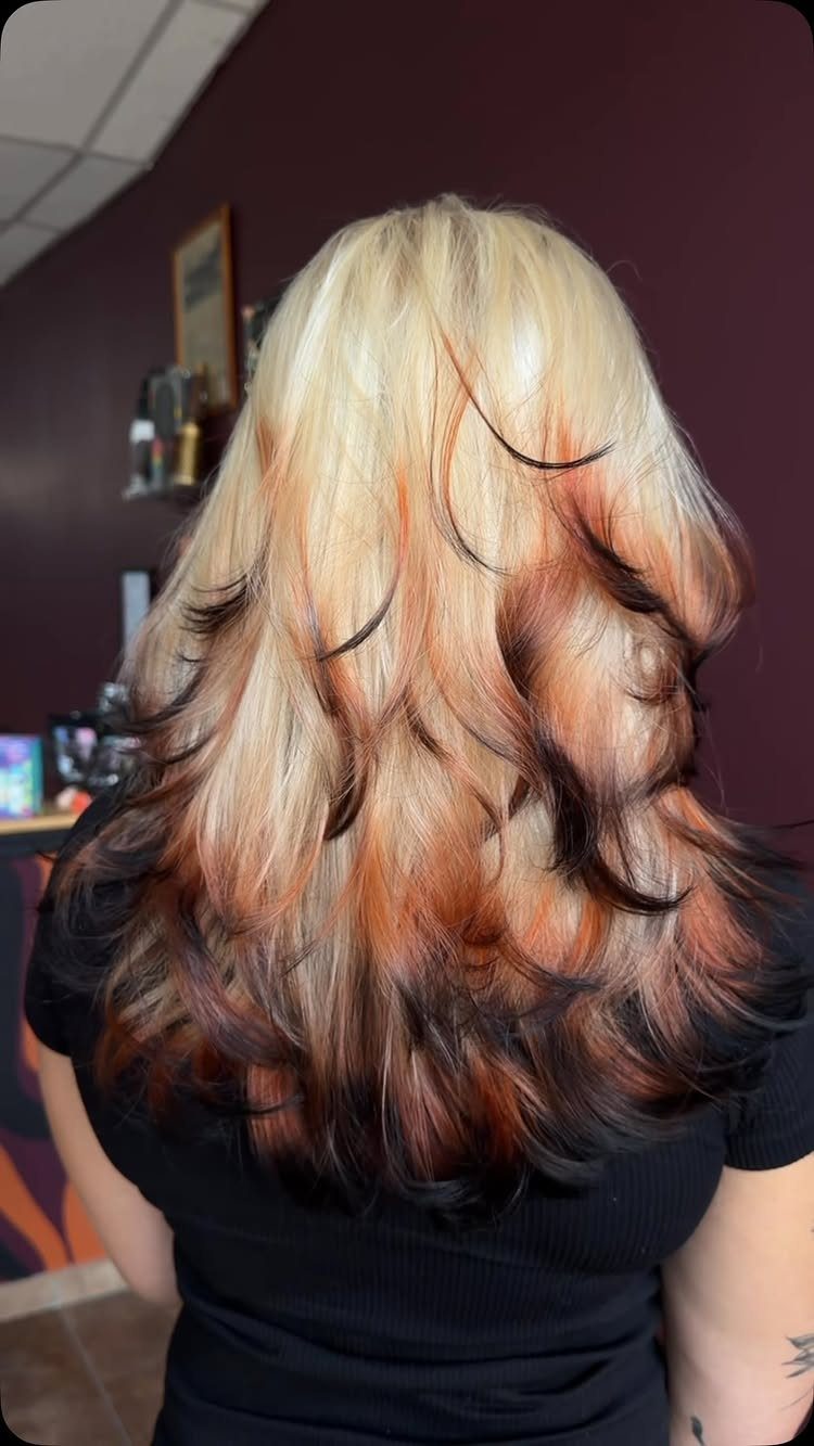Layered blonde hair with copper-orange streaks and dark roots curled at the ends