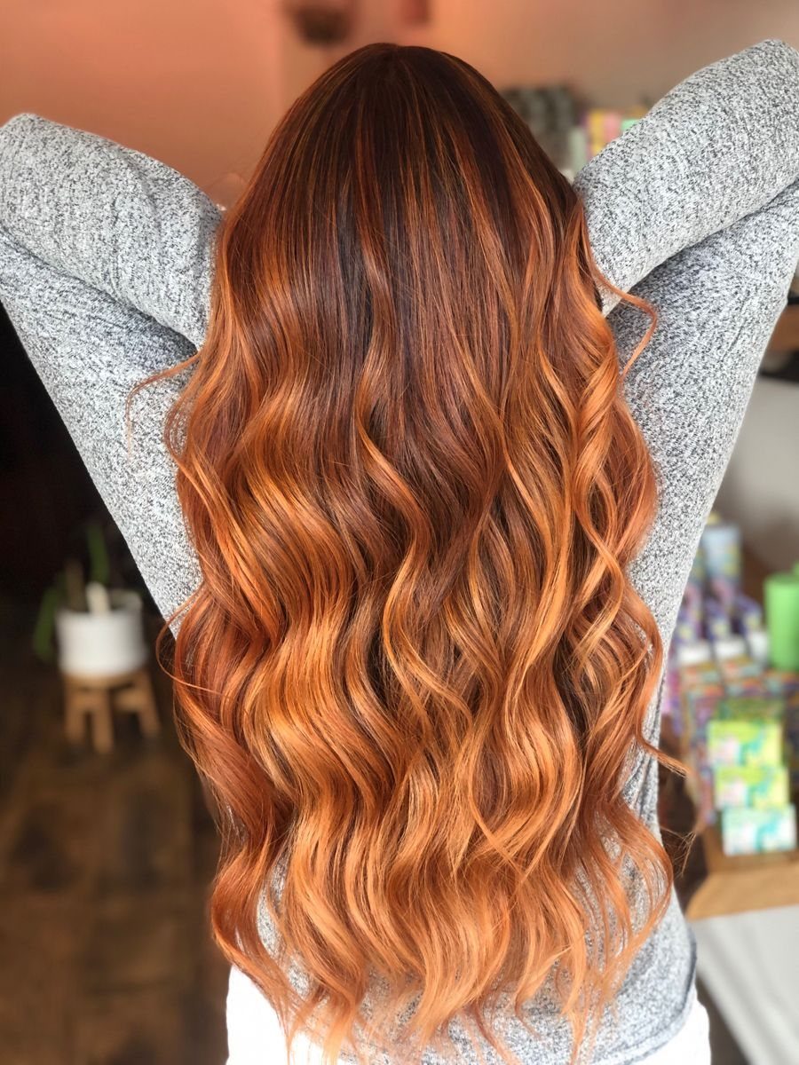 Long wavy copper-red hair with dark roots and subtle dark streaks