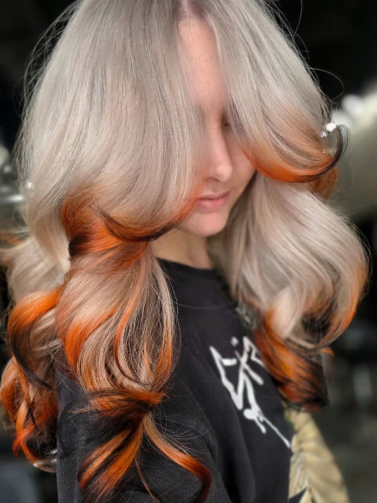 Layered blonde hair fades through copper-orange into dark, outward-curled ends