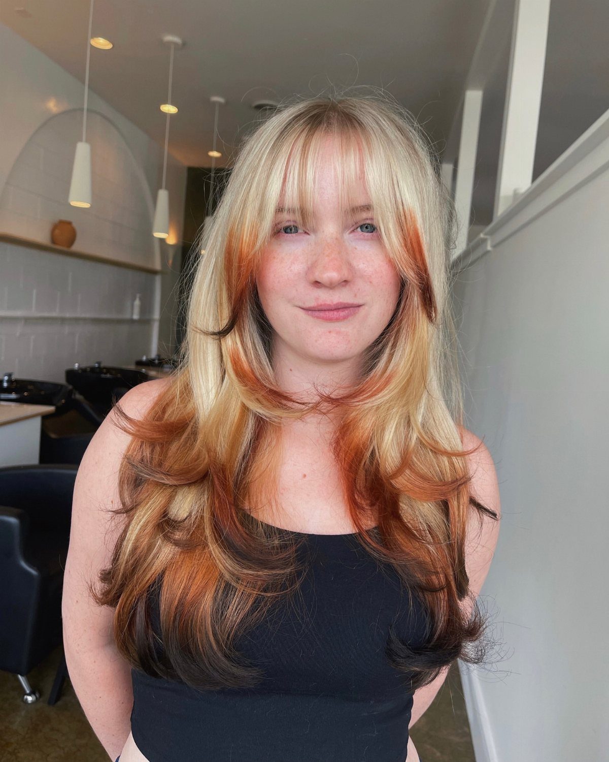 Long copper-red layered hair with dark roots and softly curled tapered ends