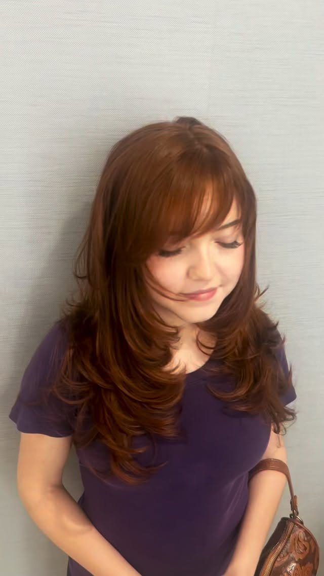Woman with layered auburn hair and bangs wearing a purple top