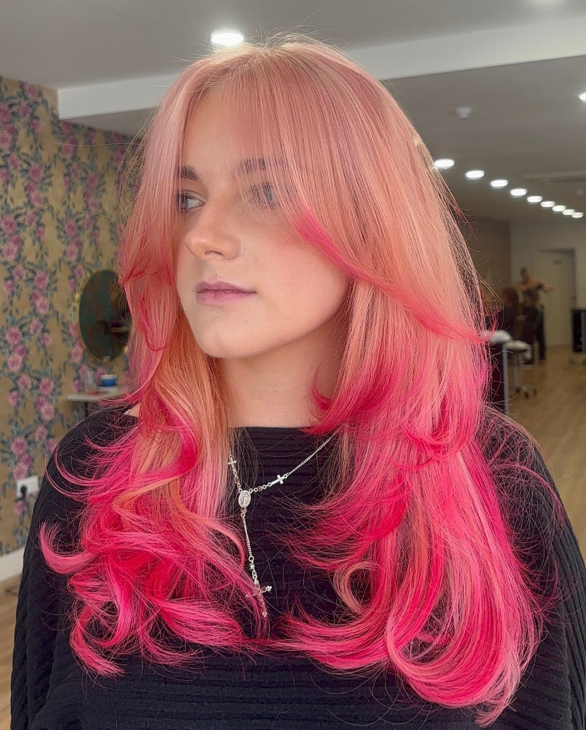 Pink layered hair with vivid curled ends frames a person in a salon