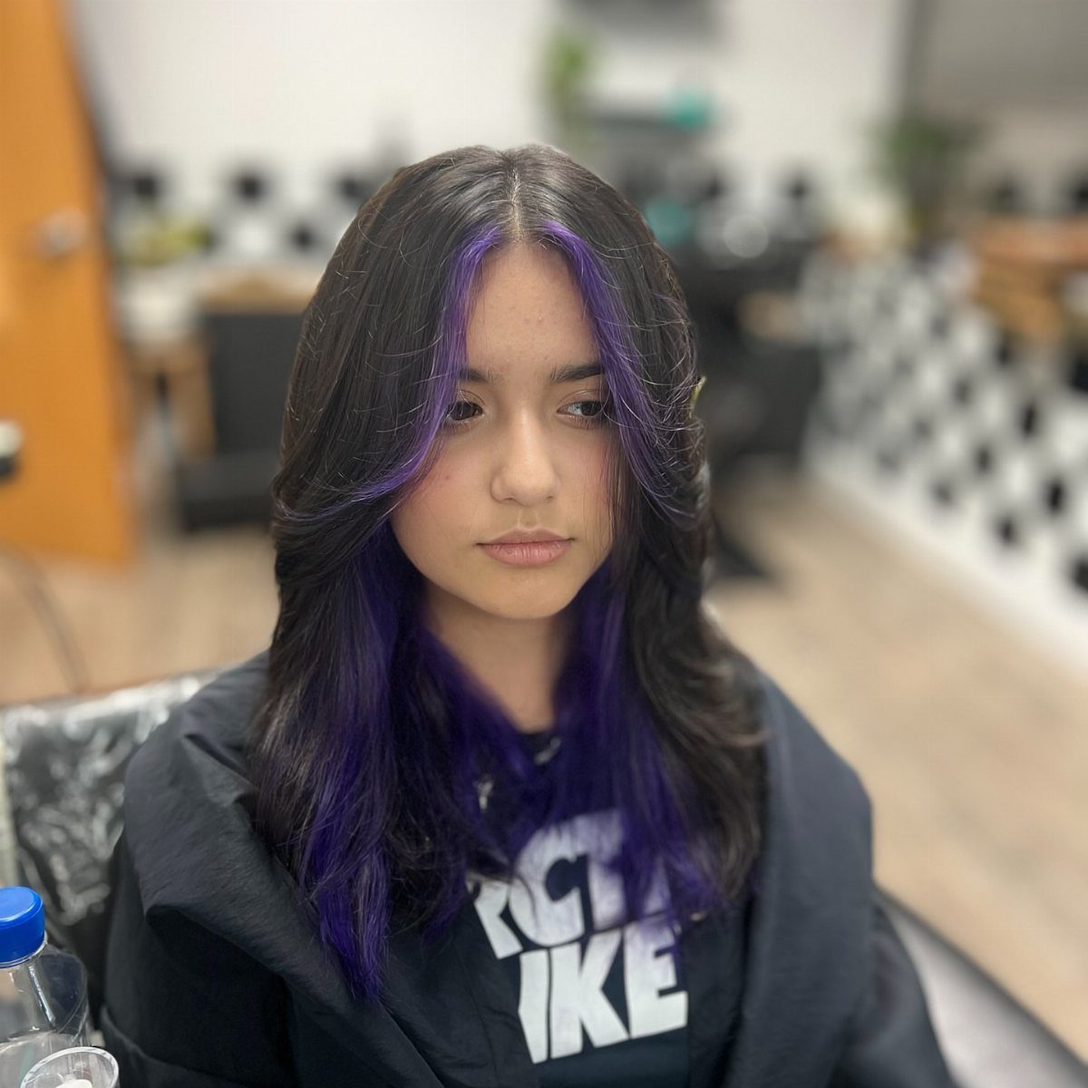 Long black layered hair with purple face-framing streaks in a salon