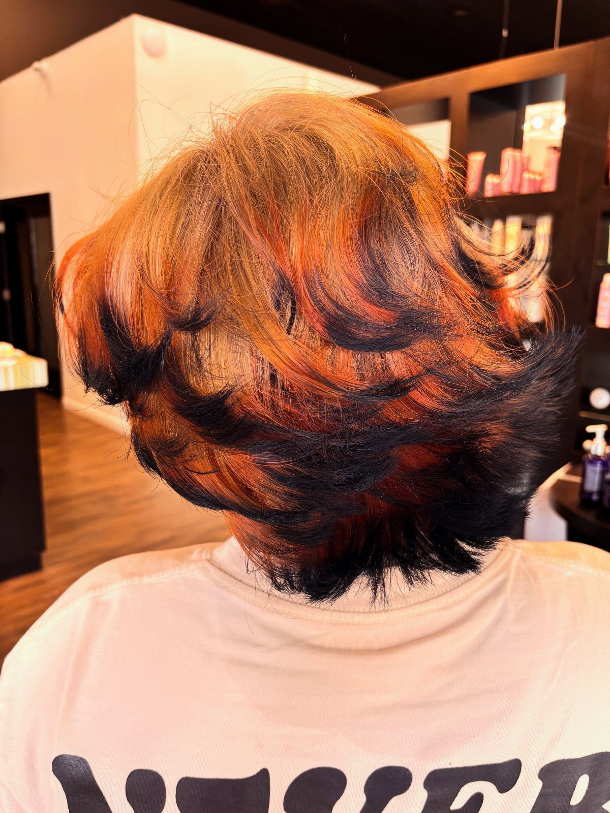 Shaggy dark layers with copper-red highlights and flipped curls in a salon