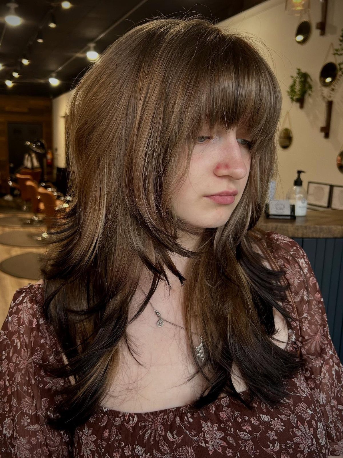 Medium-brown layered hair with wispy bangs and tapered ends in a salon