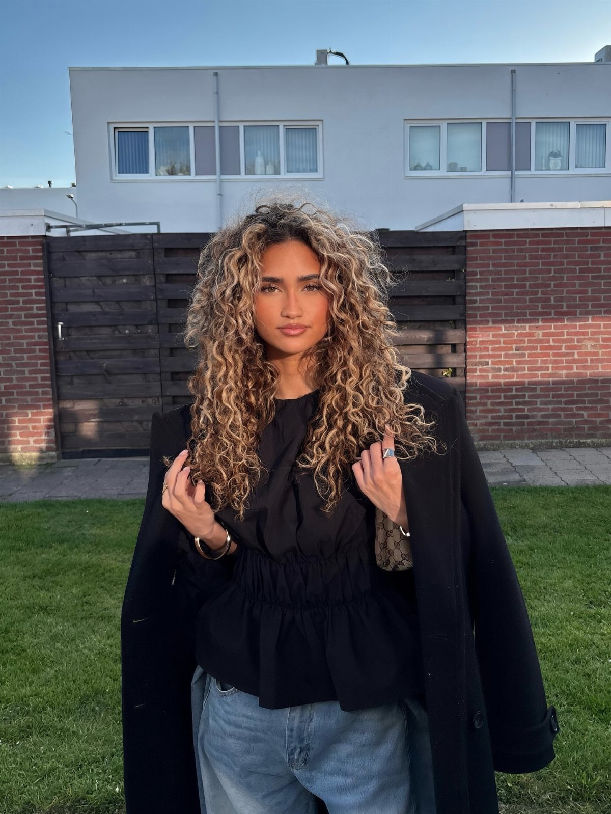 Woman with long voluminous light brown curls standing outside in a black top