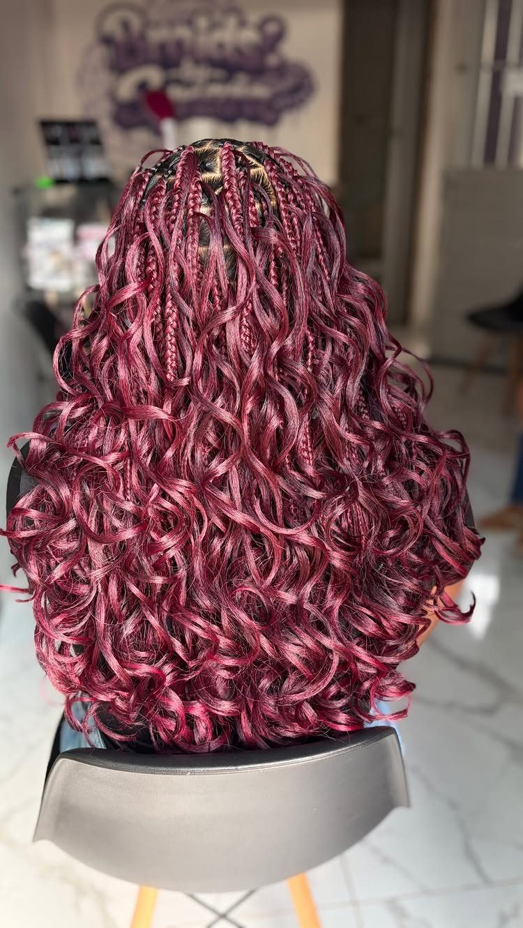 Burgundy braids with curly ends cascading down a seated salon client's back