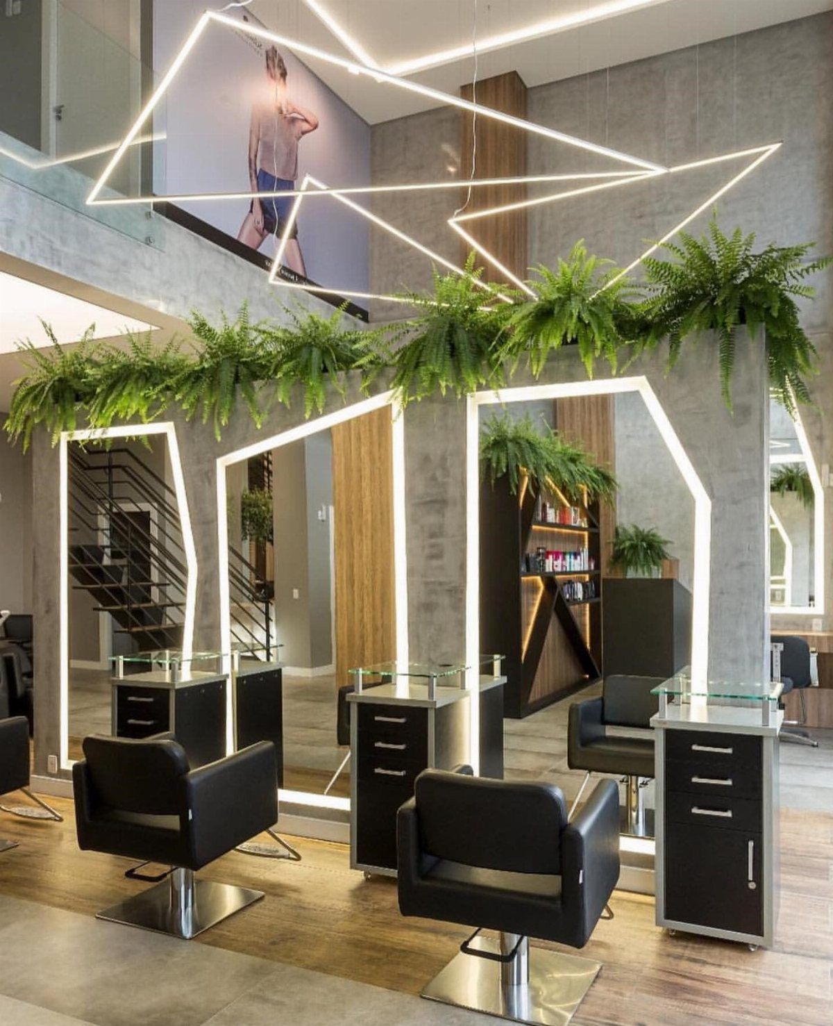 Modern salon stations with black chairs, tall mirrors, hanging ferns, and bright geometric lights