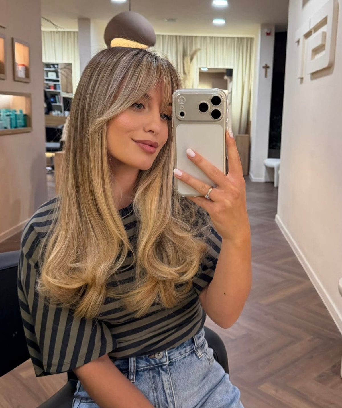 Woman showing long highlighted blonde layers and wispy curtain bangs in a salon selfie