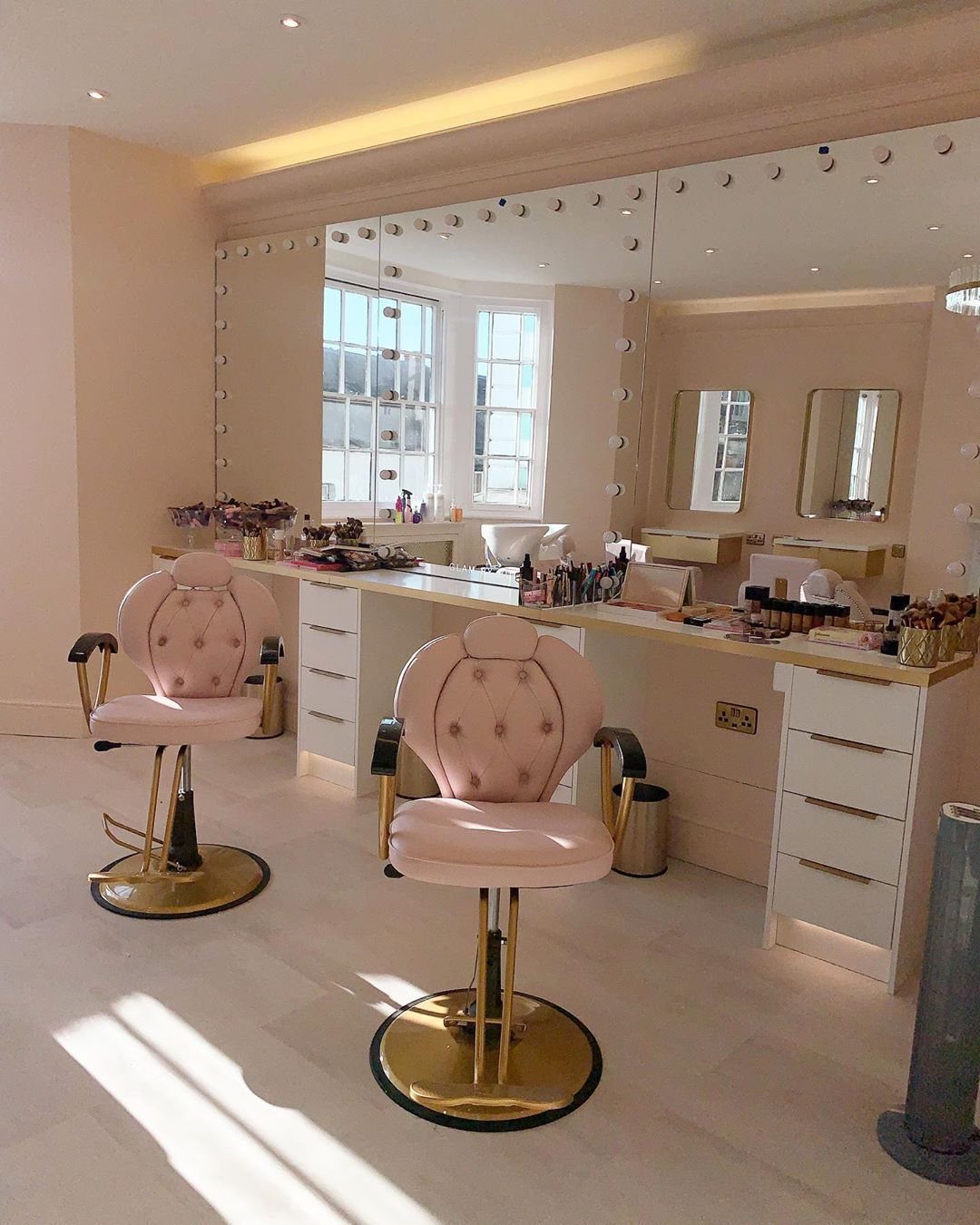 Pale pink tufted salon chairs with gold circular bases in a bright salon