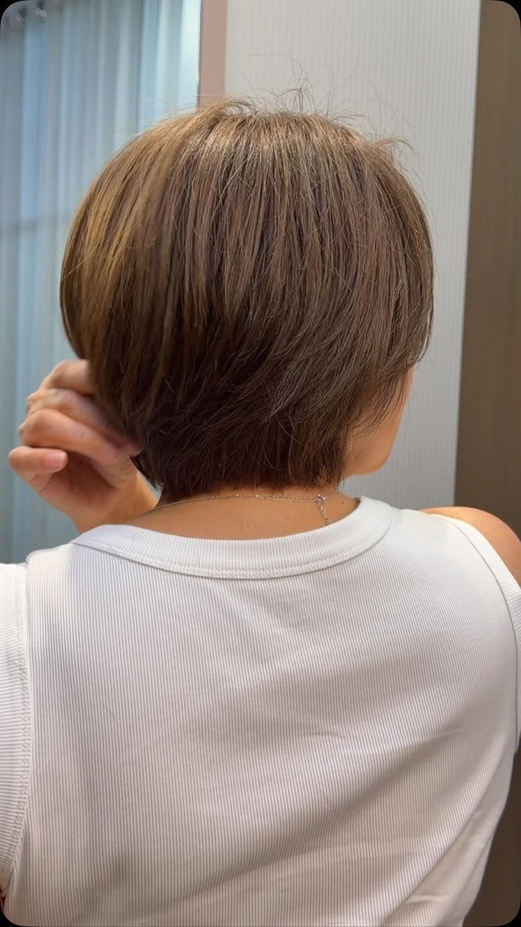 Short layered brown haircut seen from behind as the wearer touches it