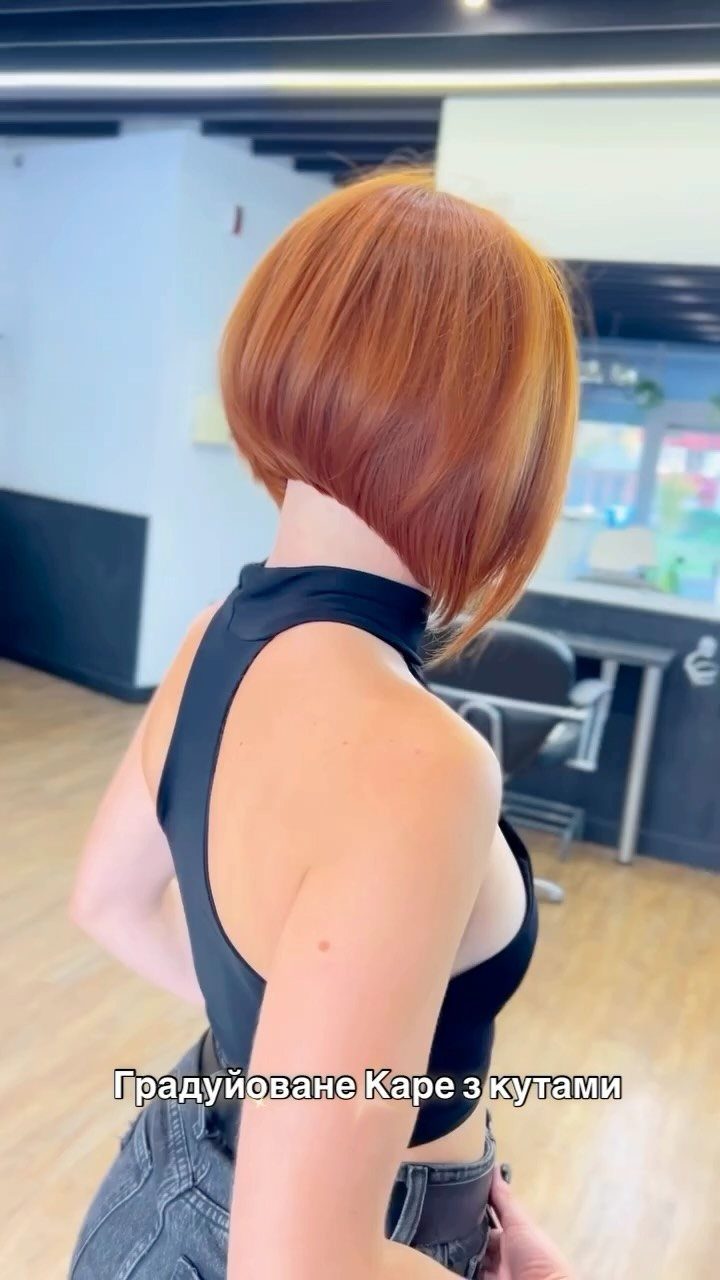 Copper-red angled bob with wispy ends, shown from the back in a salon