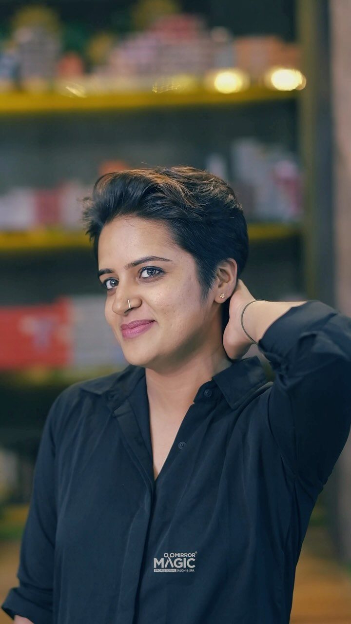 Person poses with a short, dark swept-back haircut in a black shirt