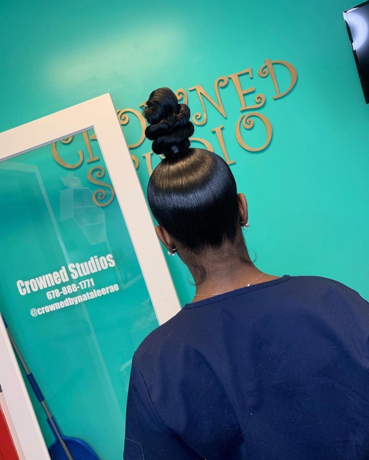 Tall coiled topknot on glossy dark hair viewed from behind at a salon
