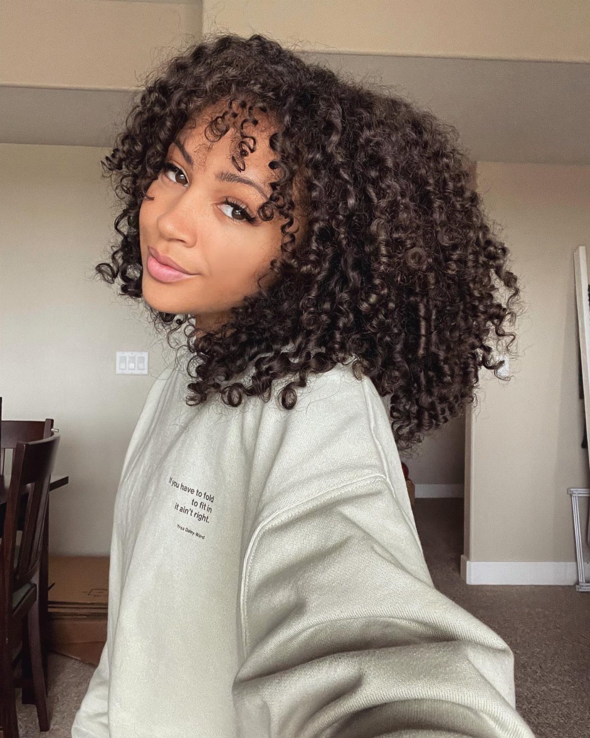 Woman showing shaped, voluminous dark curls with a light gray sweatshirt indoors