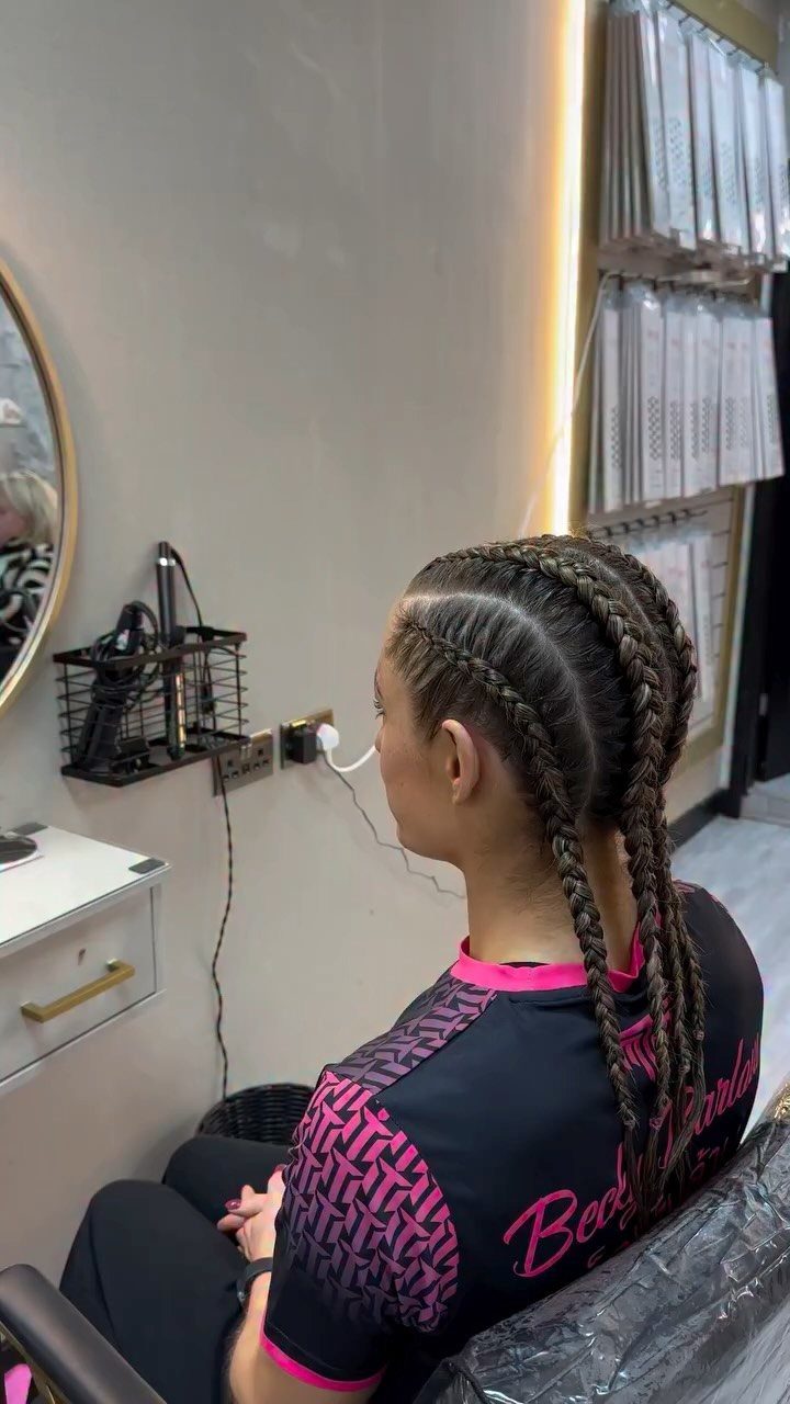 Cornrow braids gathered into long braids on a person wearing a black and pink jersey