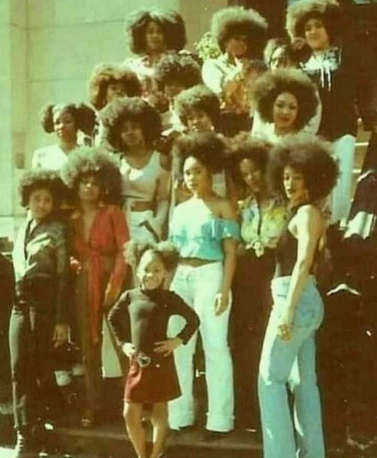Women and children pose together with rounded natural afros and colorful clothing