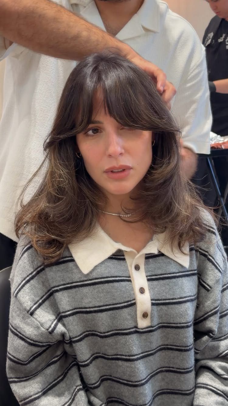 Woman with long layered dark hair and parted curtain bangs in a salon