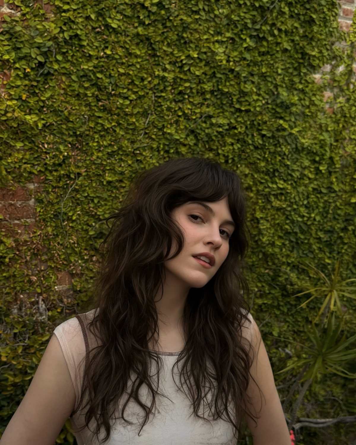 Young woman with long dark waves and bangs posing outdoors