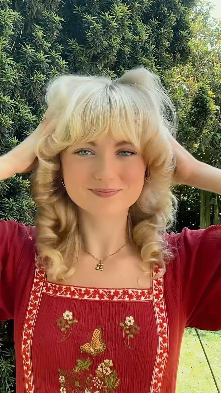 Woman with blonde voluminous curls and bangs posing in a red embroidered dress