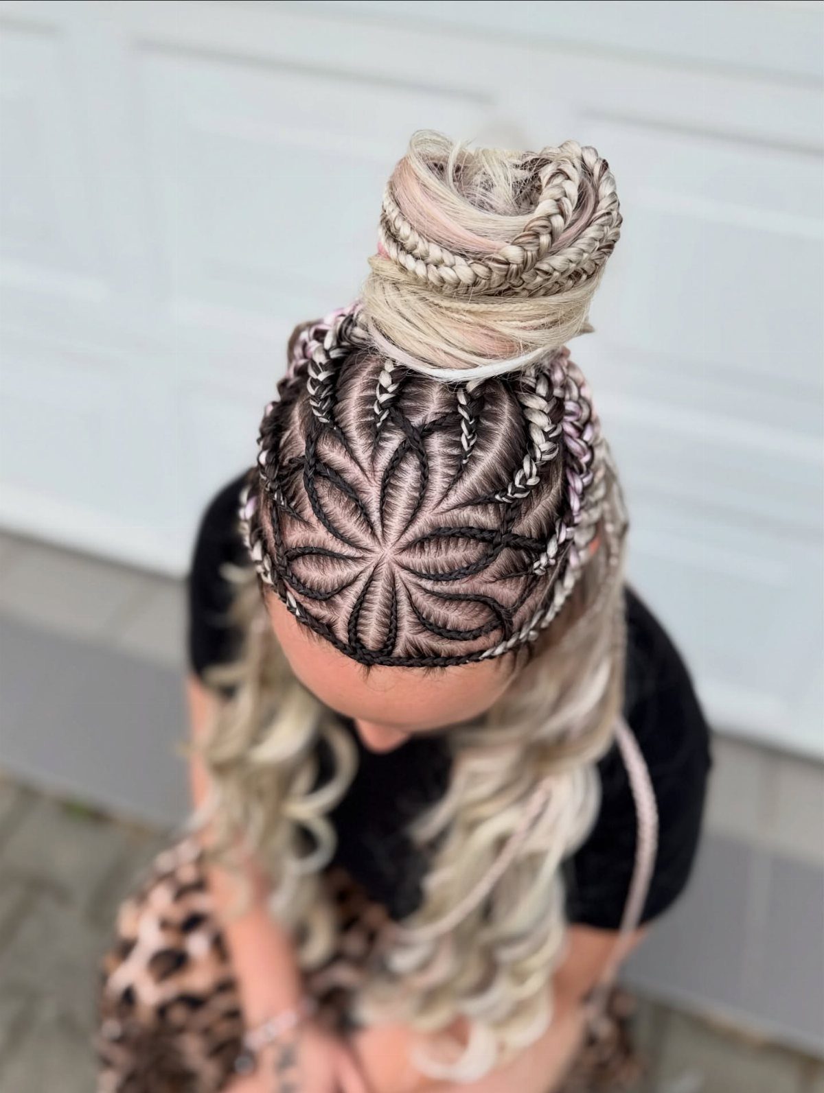 Cornrow braids form a starburst pattern beneath a blonde high bun