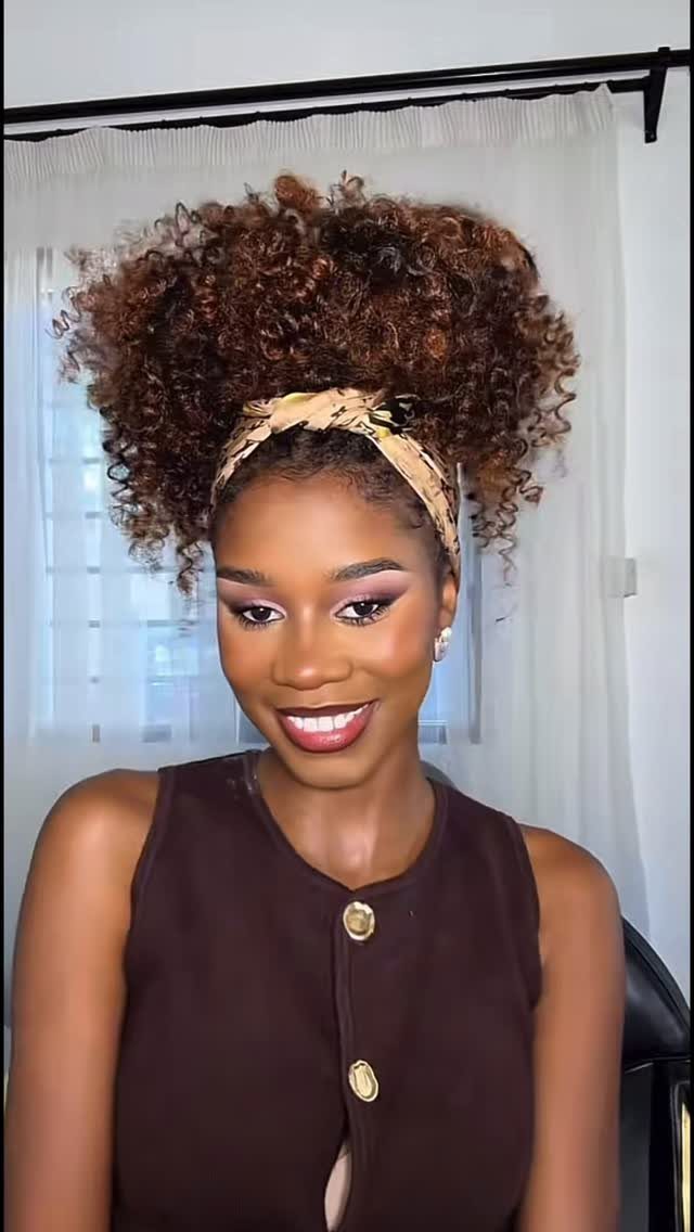 Woman wearing voluminous reddish-brown curls with a beige patterned headband