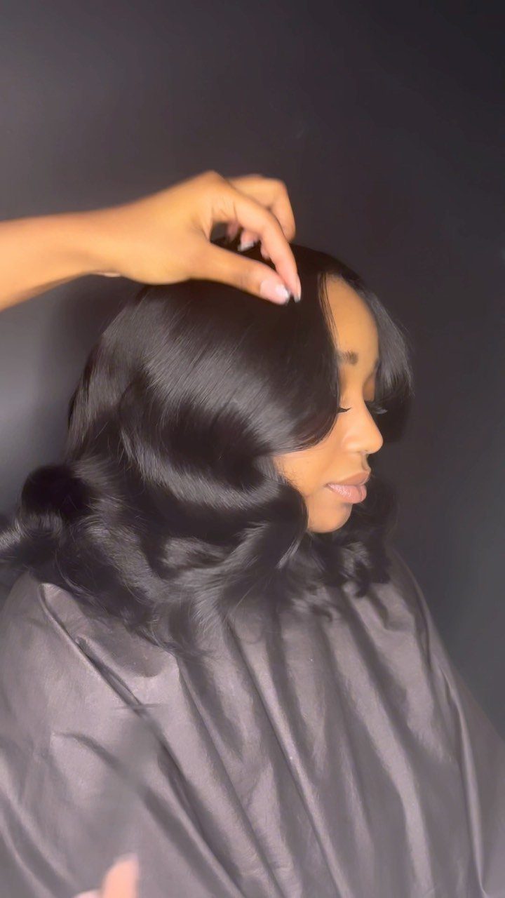 Woman with glossy black sculpted curls sits under a salon cape