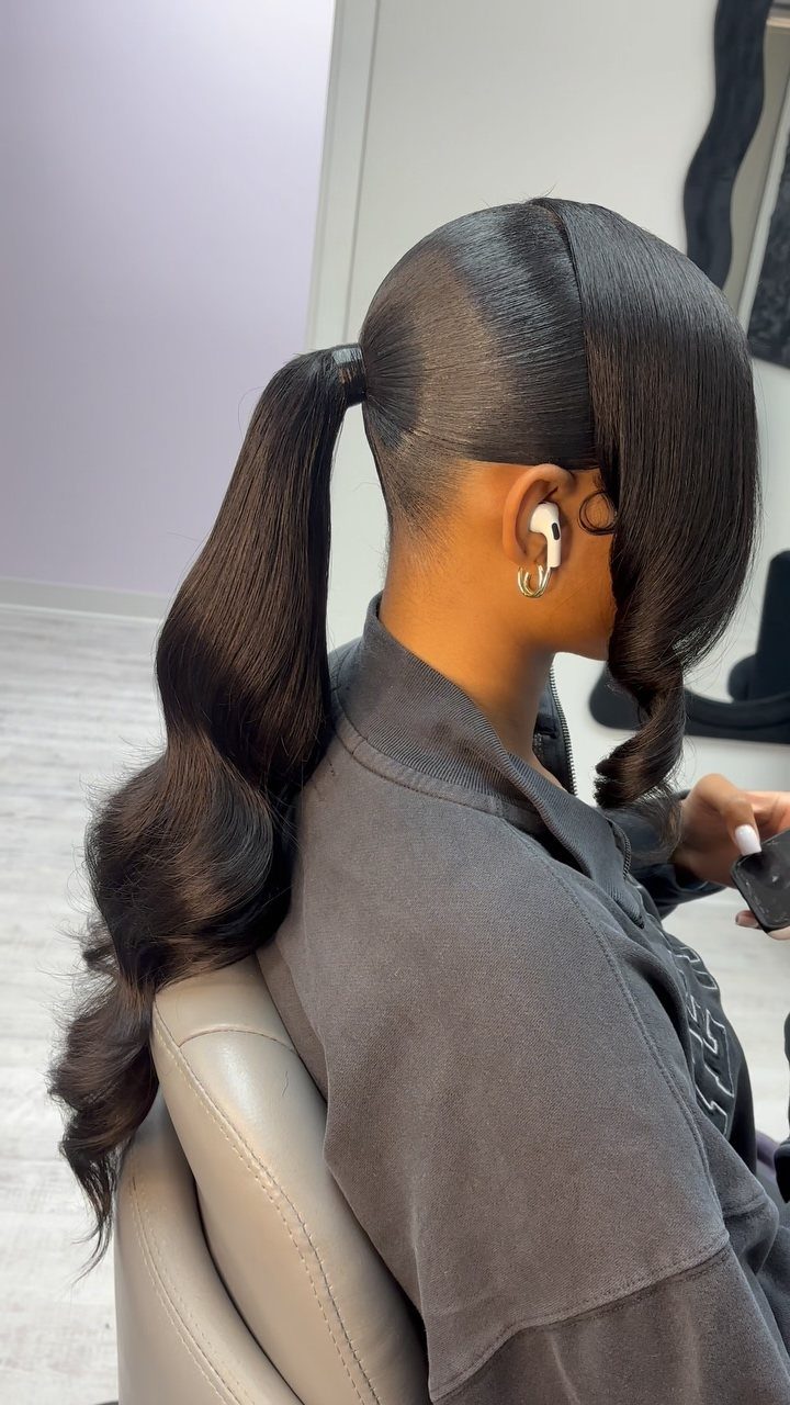 Woman with a sleek high ponytail and long curled ends seated in a salon chair