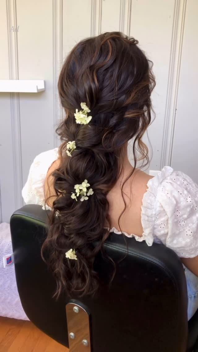 Dark twisted updo with small white flowers flowing into loose curls
