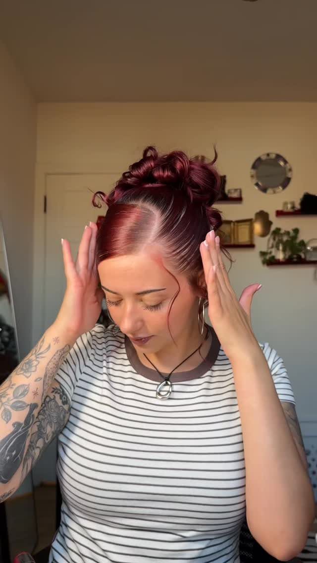 Woman smoothing her sideswept reddish hair arranged in a high curly bun
