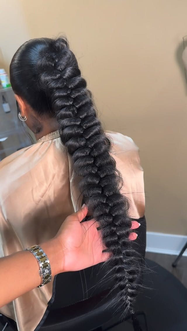 Long black ponytail braid held at the end behind a seated salon client