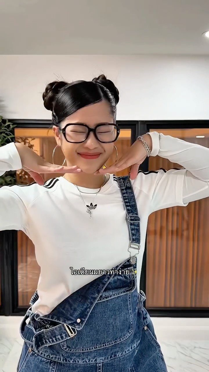 Person with glasses and denim overalls wearing two high space buns