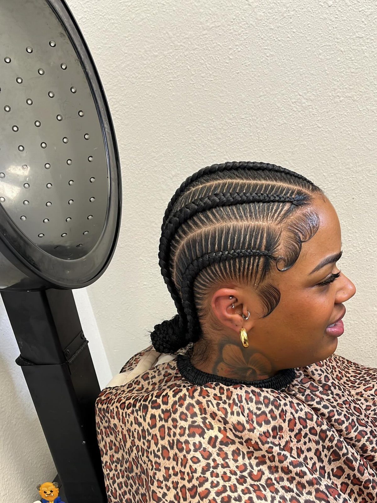 Woman with stitch braids gathered into a low ponytail beside a salon hood dryer
