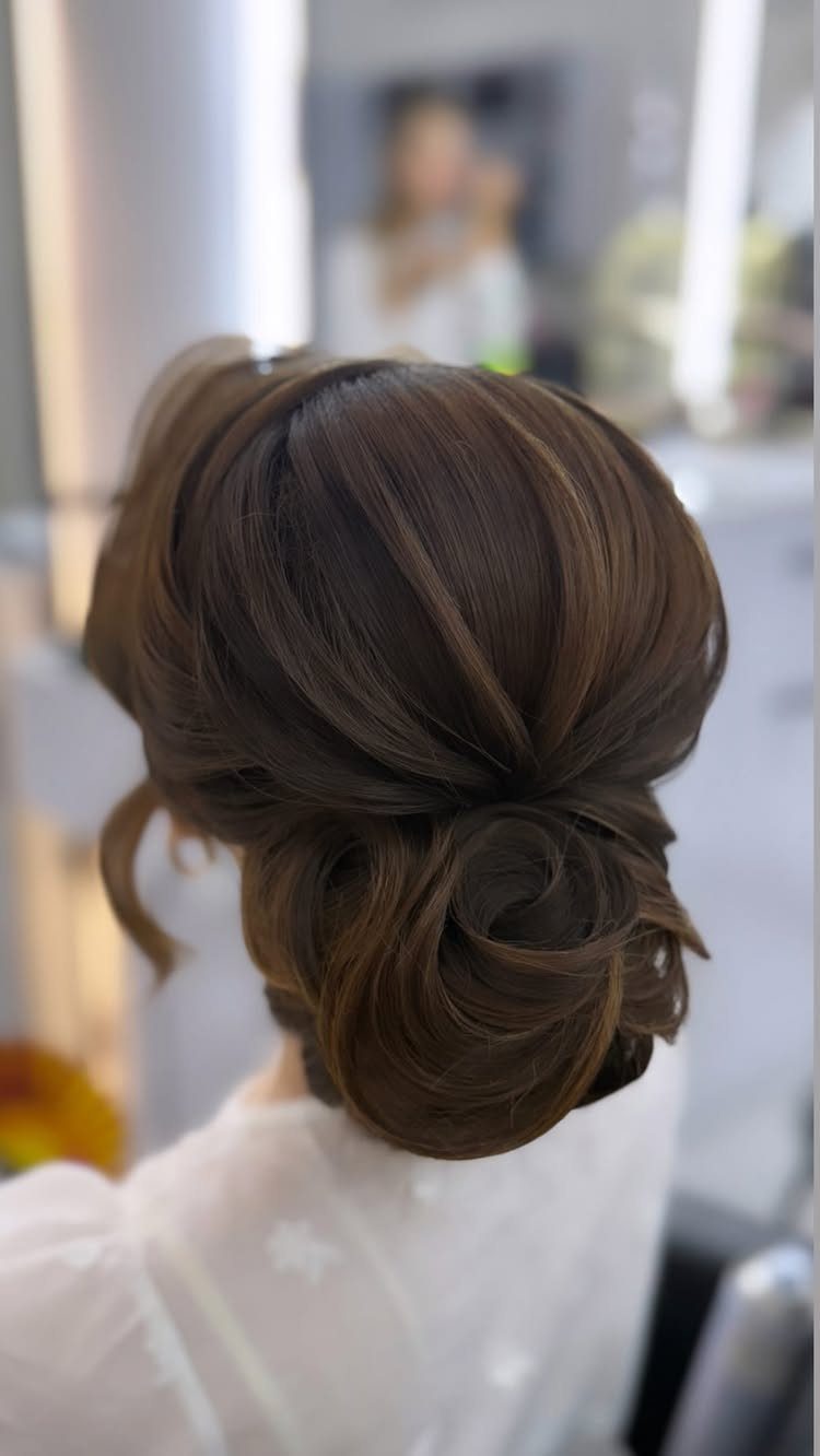 Low twisted bun with smooth dark brown hair and loose curled strands