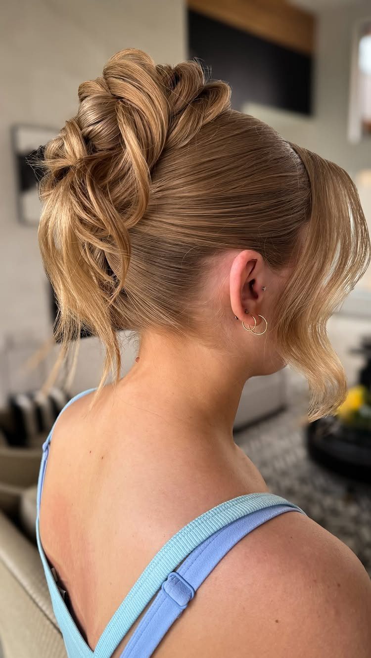 Blonde hair pinned into a voluminous wavy updo with loose curls framing her face