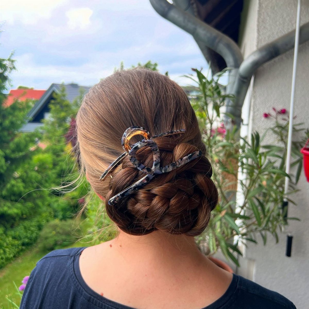 Brown braided bun secured with a claw clip, viewed from behind outdoors