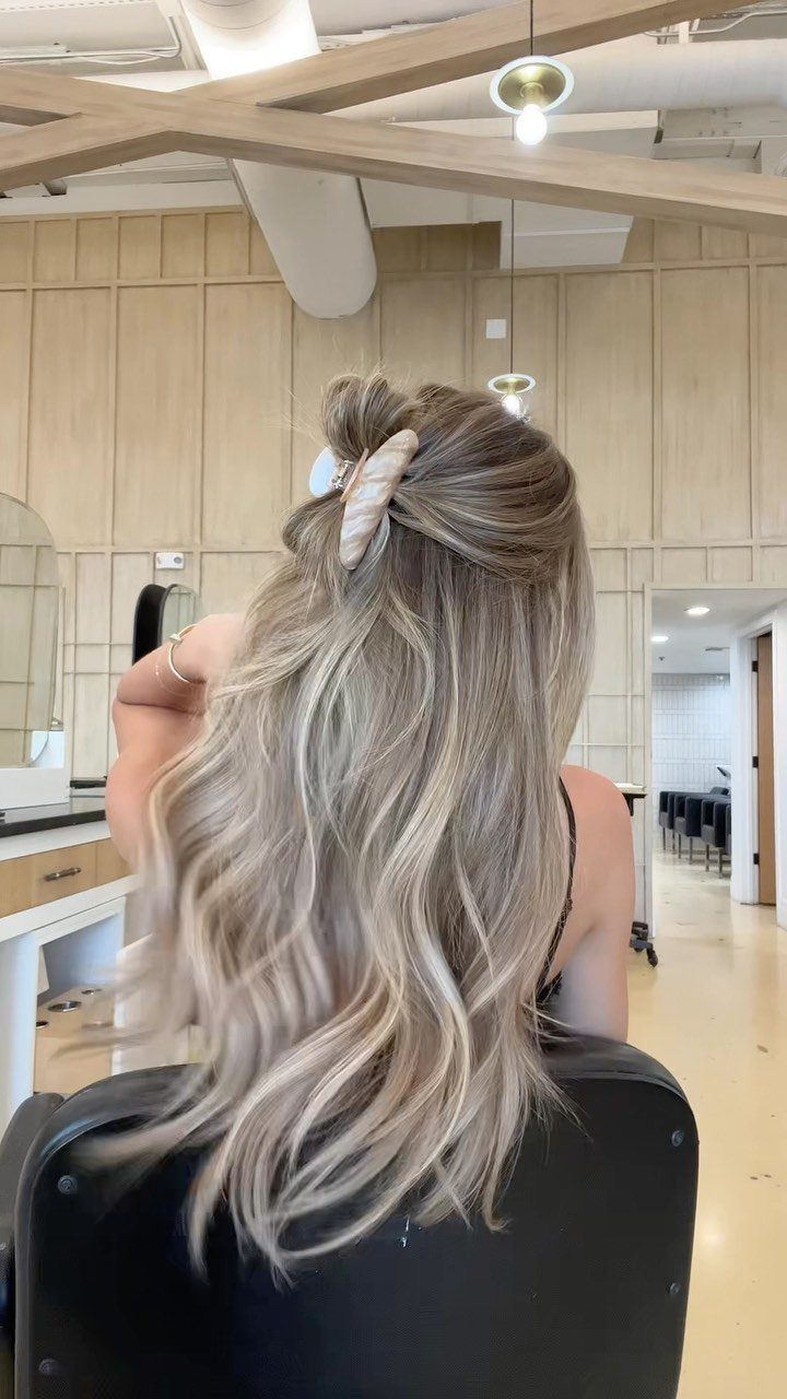 Long wavy blonde hair styled half-up in a small twisted topknot