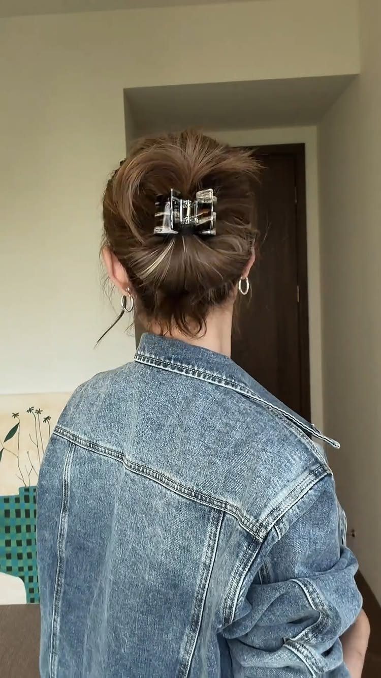 Loose brown bun secured with a silver claw clip above a denim jacket