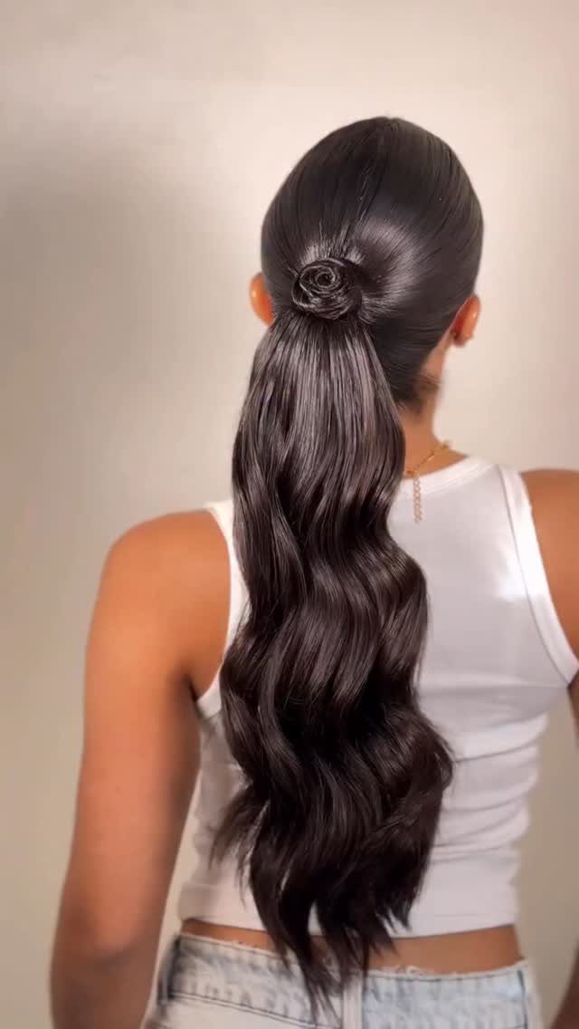 Slicked-back ponytail with long, glossy waves and a floral hair accessory