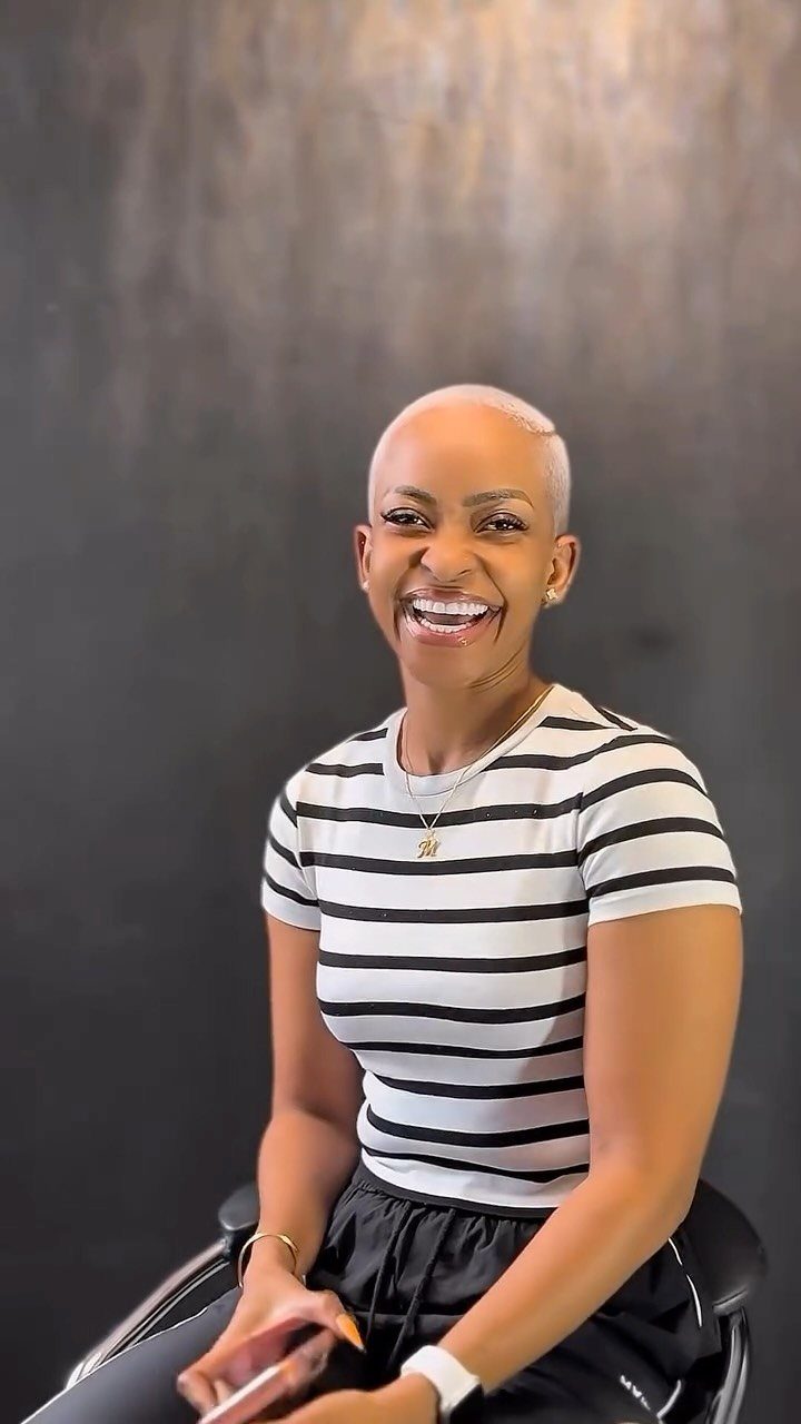 Woman with a closely cropped buzz cut smiling in a chair
