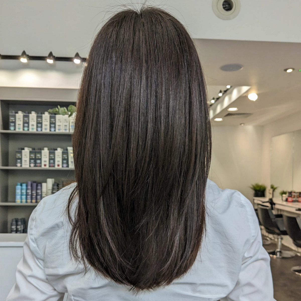Straight dark brown hair falls to the upper back in a salon