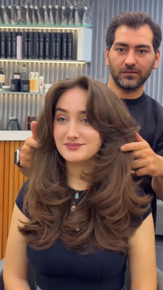 Woman displays long layered brown hair with face-framing pieces in a salon