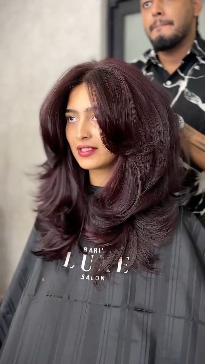 Woman showing long burgundy layered hair with face-framing pieces in a salon