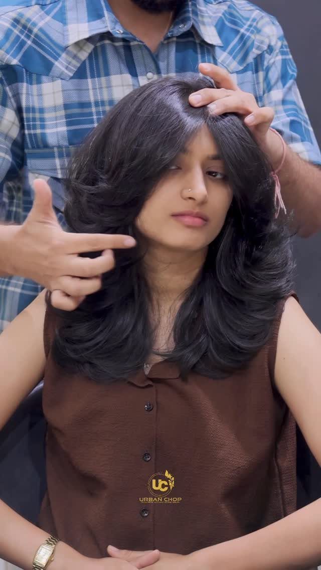 Woman with long, layered dark hair as a stylist parts and shapes it