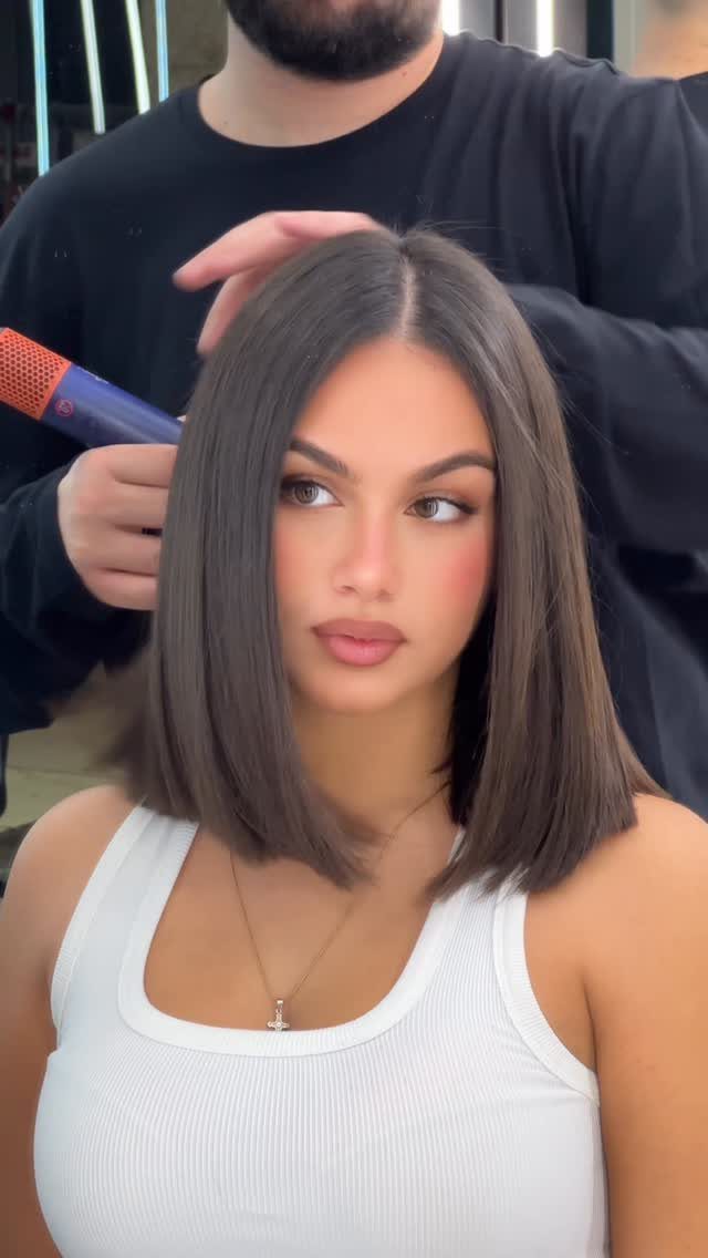 Woman with a sleek, center-parted shoulder-length brunette haircut in a salon