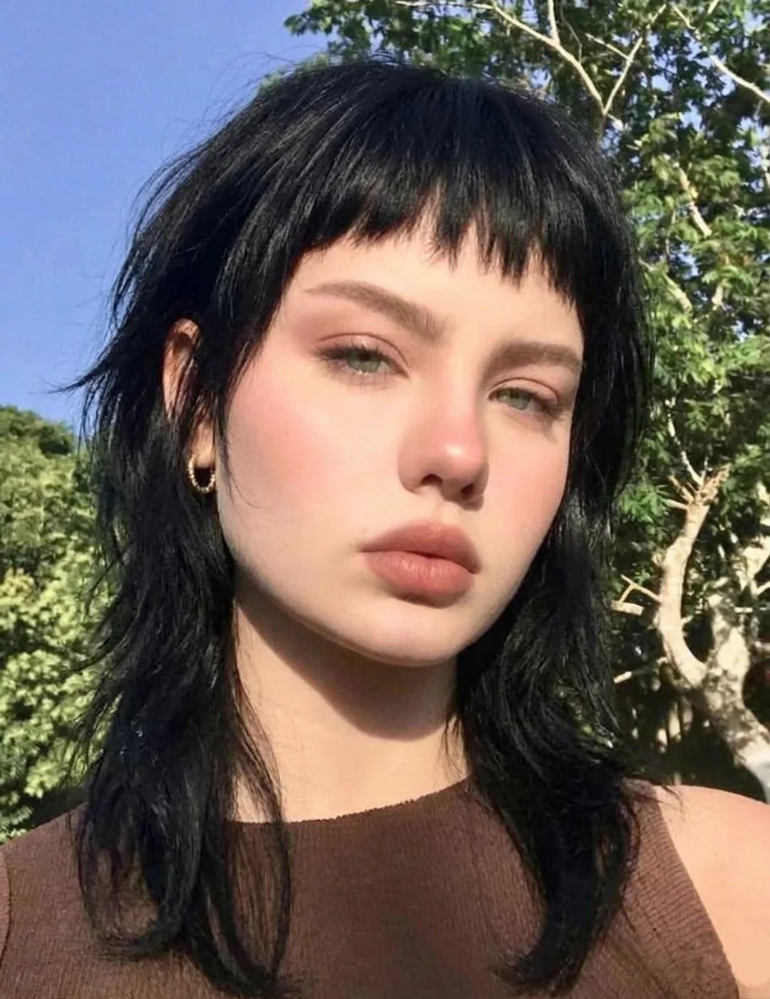 Person with dark layered hair and choppy bangs posing outdoors