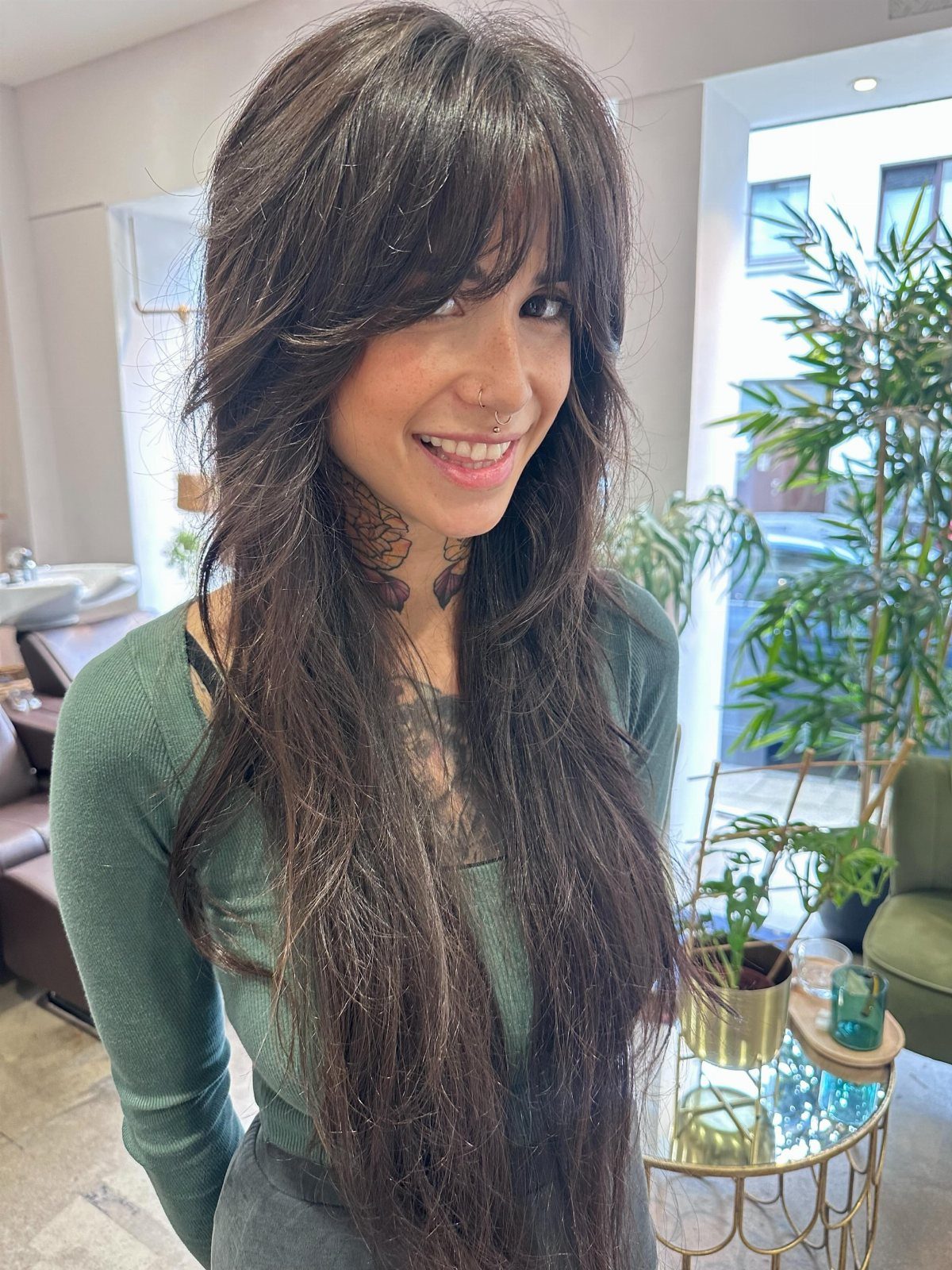 Woman with long dark wavy hair, piecey bangs, and a shaggy layered cut